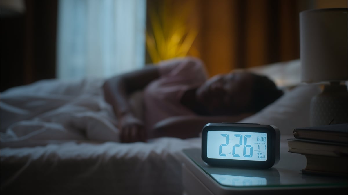 A middle-aged sleeper lies awake in bed, mildly unsettled, adjusting and searching for a comfortable position at night